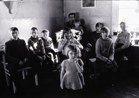 Mustavalkoinen kuva, jossa kymmenen henkilöä istuu tai seisoo huoneessa.