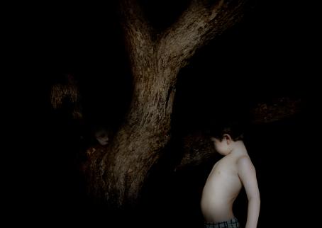 Muuten täysin musta, mutta keskellä on puu ja sen vieressä hyvin valaistu poika ilman paitaa. Puun takaa näkyy myös toiset kasvot.