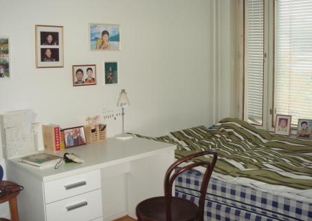 Makuuhuone, jossa ikkunan vieressä sänky, työpöytä ja seinillä valokuvia. 