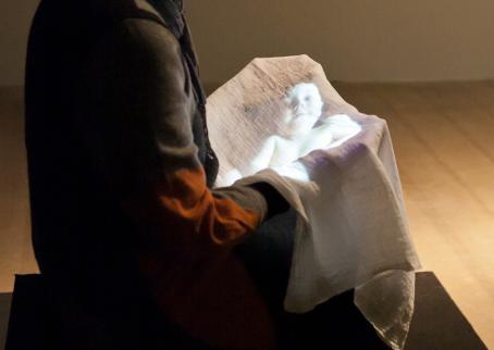 Henkilö istuu pitäen sylissään liinaa, johon heijastuu vauvan kuva. 