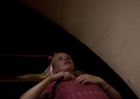 Tyttö makaa lattialla. Hänellä on hiuksissa vaaleanpunainen rusetti ja päällään vaaleanpunainen paita.