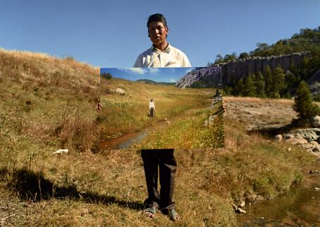 Henkilö seisoo pitäen valokuvaa, jossa on lähes samanlainen maisema kuin missä hän seisoo.