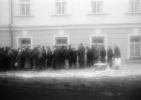 Rakeisessa, mustavalkoisessa kuvassa jono ihmisiä rakennuksen edessä.