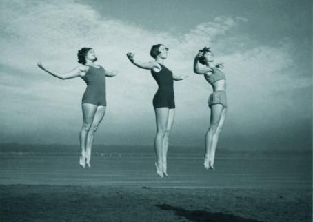 Kolme voimistelijaa hyppäämässä vierekkäin yhtä aikaa. Taustalla näkyy ranta ja vettä.
