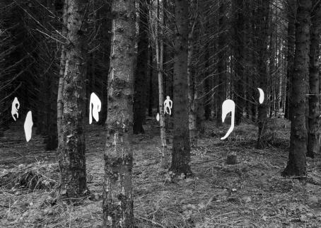 Mustavalkoisessa kuvassa metsässä puiden välissä on valkoisia hahmoja, osa hieman ihmisen muotoisia, osa muodottomia möykkyjä.