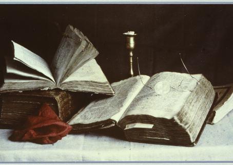 Kasassa on neljä kirjaa, joista kaksi on avoinna. Toisen avoimen kirjan päällä on silmälasit. Taustalla näkyy loppuunpoltettu kynttilä messinkisessä kynttilänjalassa.