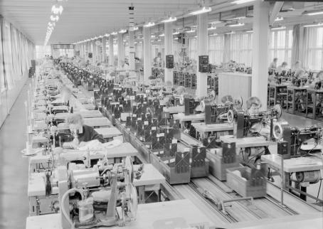 Näkymä isosta tehtaasta, missä työntekijät ompelevat ompelukoneilla.